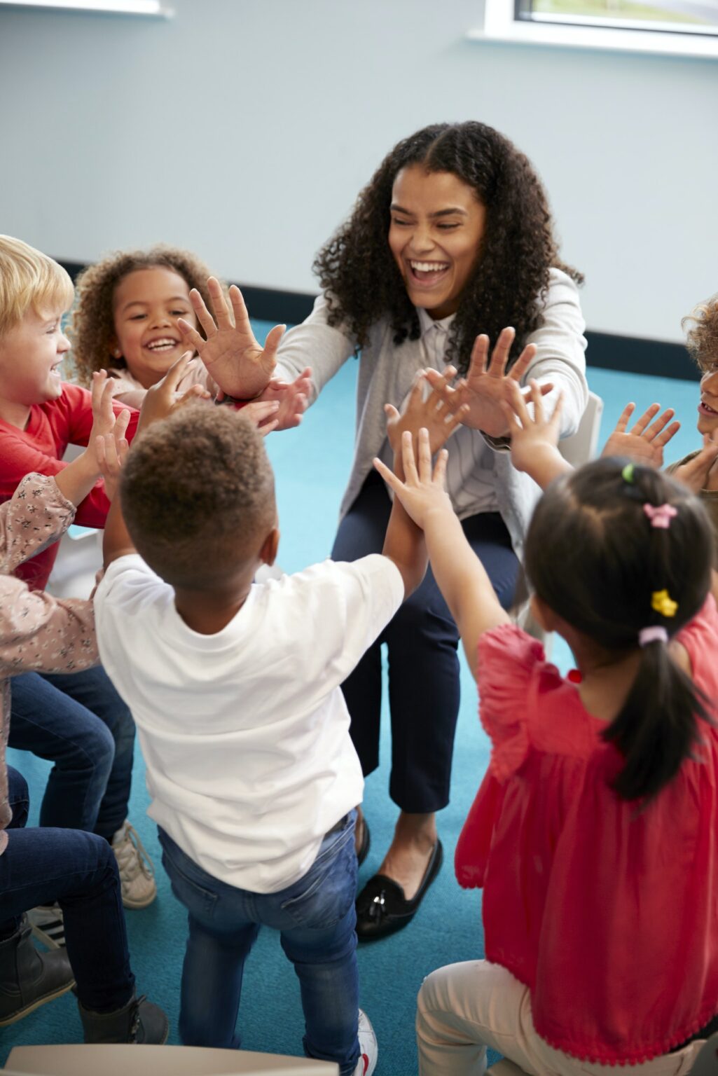 infant-school-children-in-a-circle-in-the-classroom-giving-high-fives-to-their-teacher-1025x1536